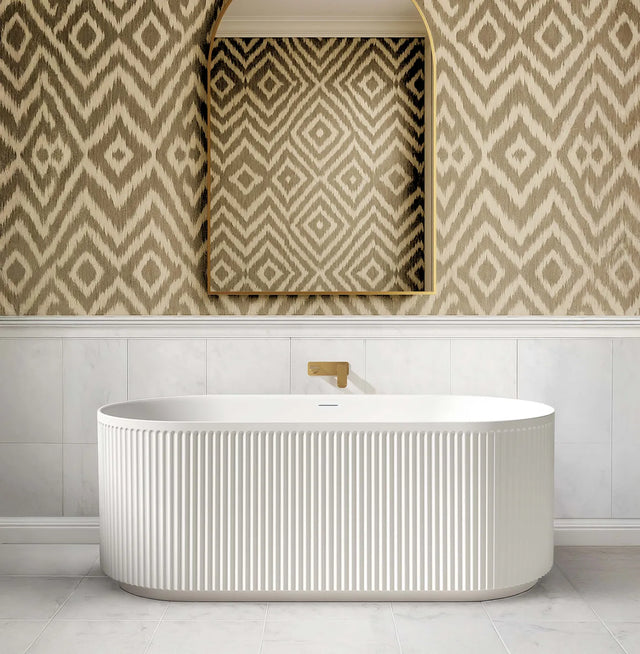 Modern freestanding bathtub in a bathroom with patterned wallpaper and mirror.