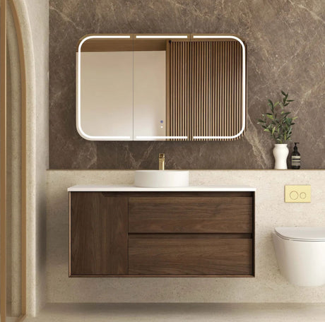 Bathroom vanity with wooden cabinet, mirror, and sink against a marble wall.