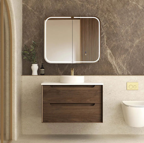 Bathroom setup with wooden vanity, mirror, and toilet against a marble wall.