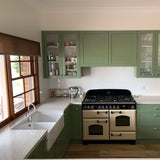 Modern kitchen with green cabinets, white countertops, and a brick wall.