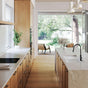 Modern kitchen with wooden cabinets, white countertops, and a view of greenery outside.