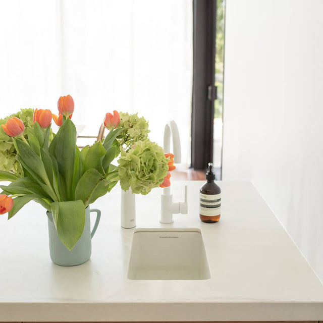 Kitchen counter with flowers and a bottle, featuring a window in the background.