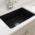 White kitchen sink with black grid and silver faucet on a marble countertop.