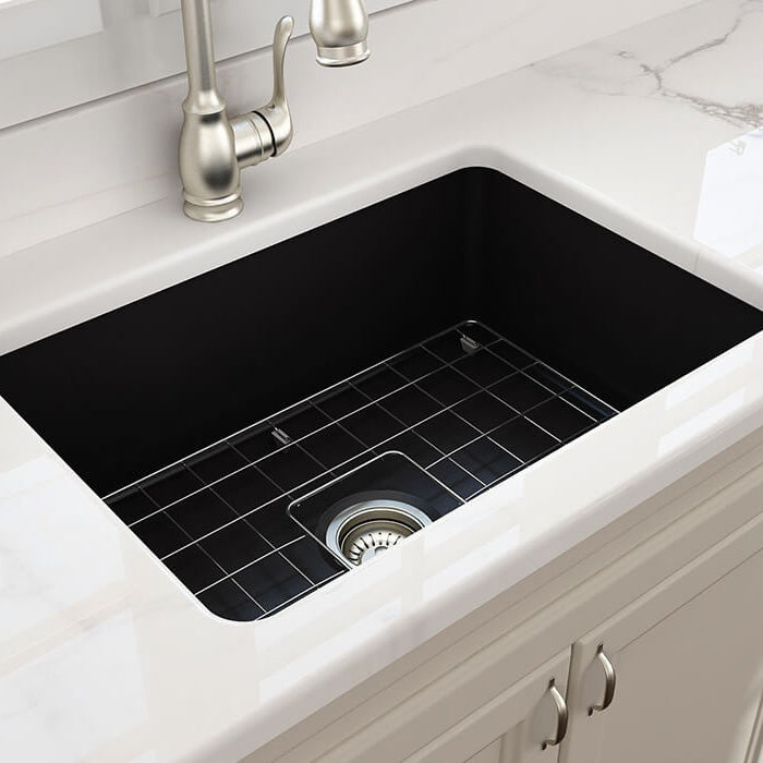 White kitchen sink with black grid and silver faucet on a marble countertop.