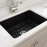 White kitchen sink with black grid and silver faucet on a marble countertop.