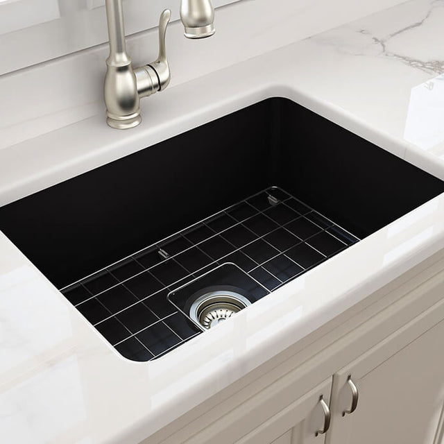 White kitchen sink with black grid and silver faucet on a marble countertop.