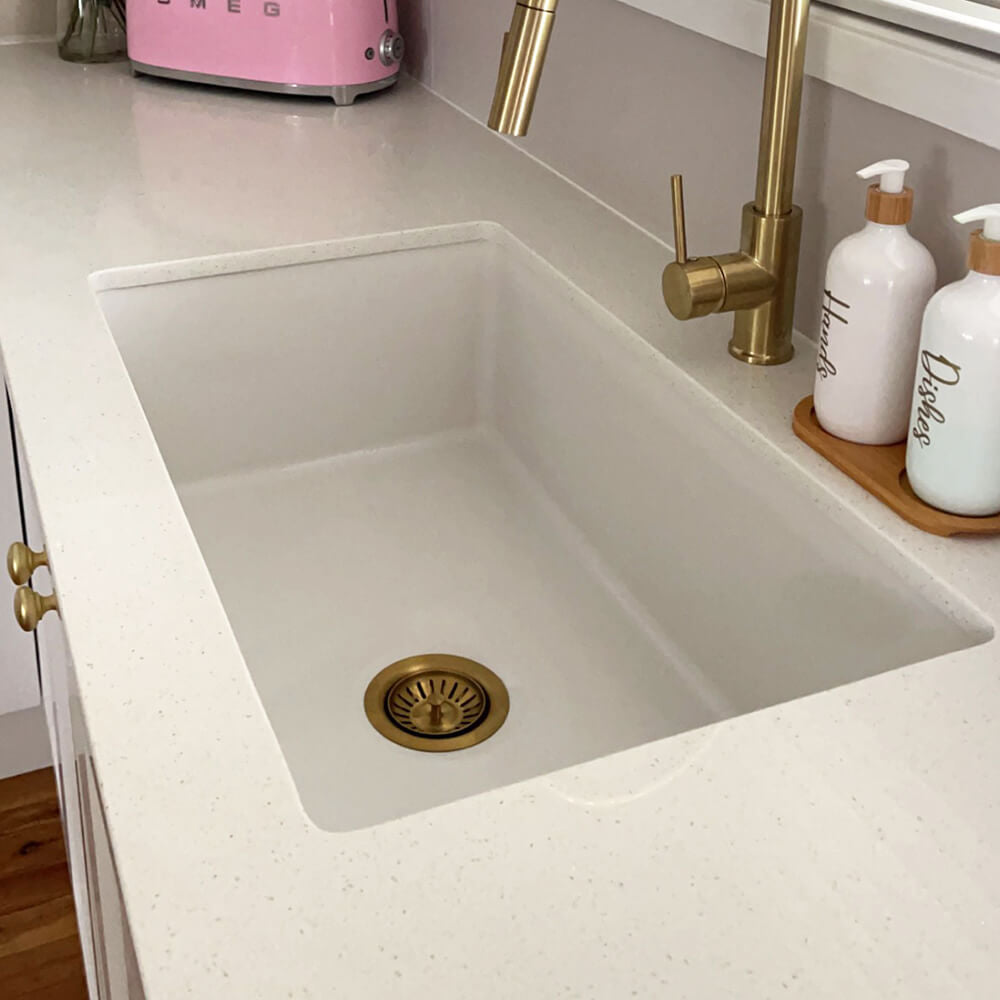 Modern kitchen with white sink, gold faucet, and pink Smeg toaster.