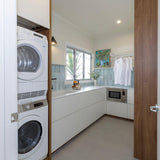 Modern laundry room with stacked washer and dryer, white cabinets, and a wooden door.