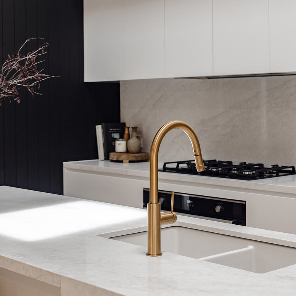 Modern kitchen with a gold faucet over a sink, black stove, and white cabinets.