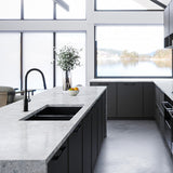 Modern kitchen with black cabinets, white countertops, and a view of water through large windows.