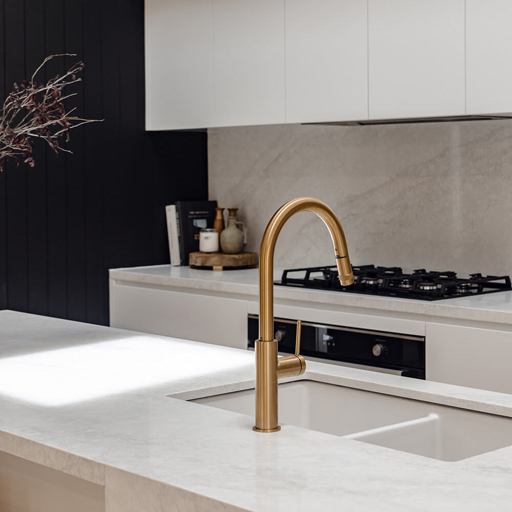 Modern kitchen with a gold faucet over a sink, black stove, and white cabinets.