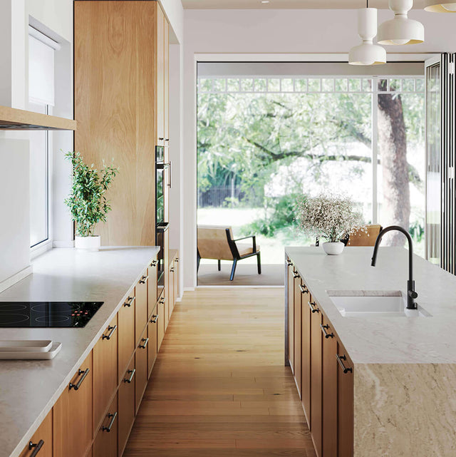 Modern kitchen with wooden cabinets, white countertops, and a view of greenery outside.