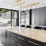 Modern kitchen with dark cabinets, marble countertop, and gold fixtures.