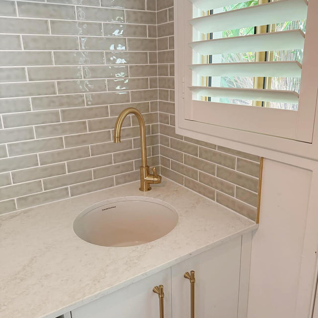 Bathroom corner with a sink, gold faucet, and white cabinets.
