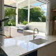 Modern kitchen with white marble countertop, sink, and grill area with large windows overlooking greenery.