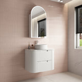 Bathroom with a white vanity unit, sink, and mirror against a tiled wall.