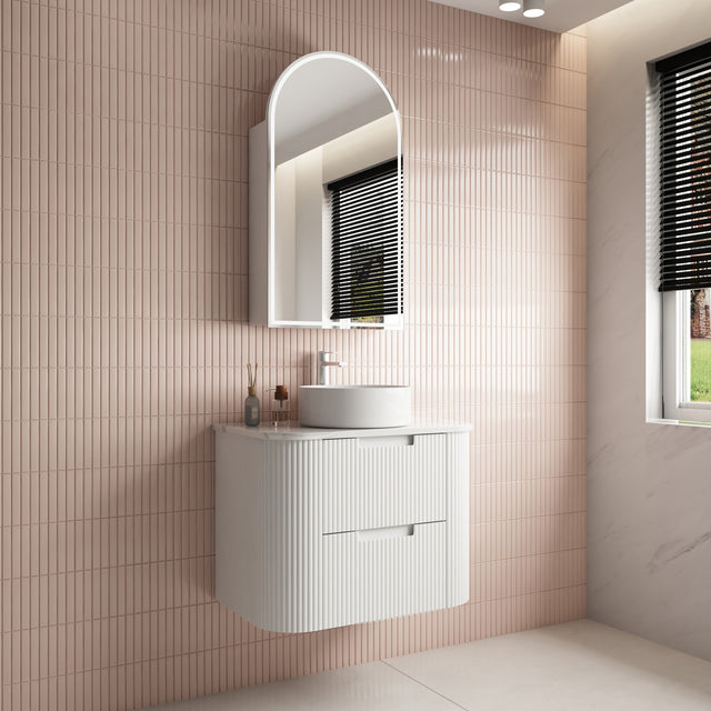 Bathroom with a white vanity unit, sink, and mirror against a tiled wall.