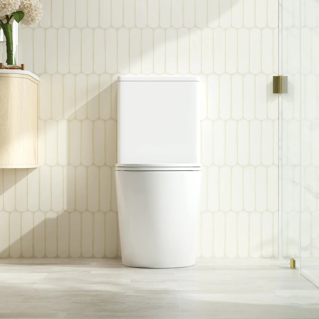 A modern two-piece white toilet with a closed lid, set against a beige hexagonal tiled wall in a brightly lit bathroom.