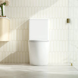 A modern two-piece white toilet with a closed lid, set against a beige hexagonal tiled wall in a brightly lit bathroom.
