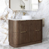 A modern bathroom vanity with a fluted wood cabinet, white countertop, white vessel sink, and a matching wall-mounted mirror, set against a white marble wall and floor.