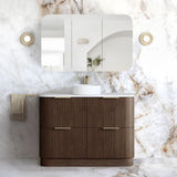A modern bathroom vanity set featuring a dark brown ribbed cabinet with gold handles, a white countertop, a white vessel sink, a matching wall mirror, and a white marble-look wall and floor in a luxury bathroom setting.