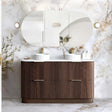 A modern double-sink bathroom vanity with a fluted dark wood cabinet, white countertop, and two white vessel sinks, set against a white marble wall with an oval mirror and wall sconces.