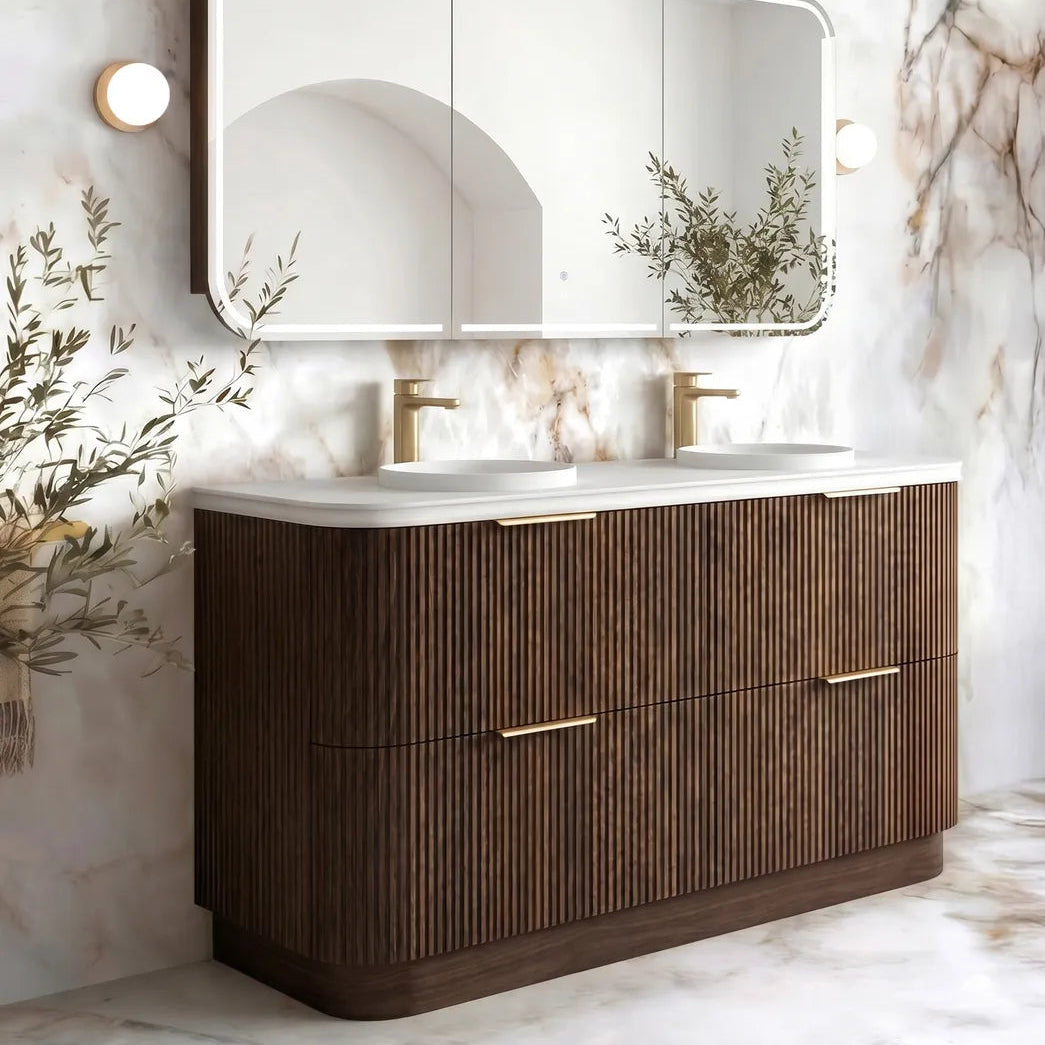A modern double-sink bathroom vanity with a dark brown ribbed wood cabinet, white countertop, and a large three-panel mirror mounted on a marble-patterned wall.
