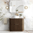A modern bathroom vanity set featuring a ribbed brown wooden cabinet with a white ceramic vessel sink, a white wall-mounted mirror, and a marble-look wall and floor in a bright, styled bathroom setting.