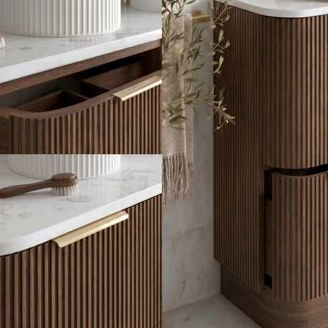 A modern bathroom vanity setup with fluted dark brown wood cabinets, white marble countertops, gold faucets and handles, and a matching fluted storage cabinet. A white vessel sink, a wooden brush, and a hanging olive branch decor element are visible.