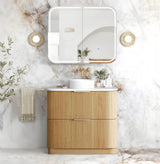A modern bathroom vanity set featuring a ribbed light wood cabinet with a white countertop, a white vessel sink, and a matching white medicine cabinet with a mirror, set against a white marble wall.