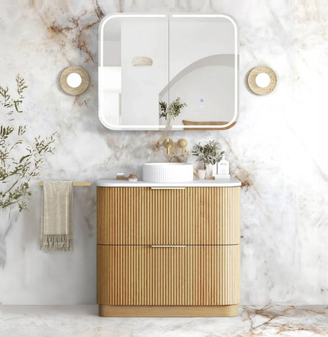 A modern bathroom vanity set featuring a ribbed light wood cabinet with a white countertop, a white vessel sink, and a matching white medicine cabinet with a mirror, set against a white marble wall.