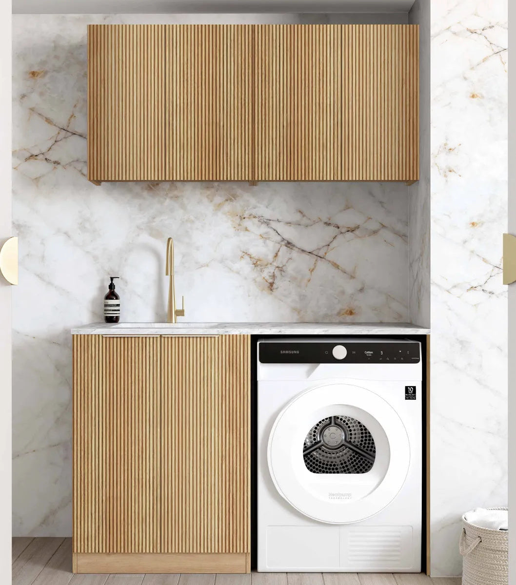 A modern laundry room setup featuring a white front-load washing machine integrated into a slatted wood cabinet, set against a white marble backsplash and light wood flooring.