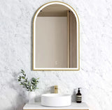 Arch-shaped mirror with gold frame on a marble wall above a sink.