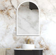 Bathroom with marble wall, white sink, and arch-shaped mirror.
