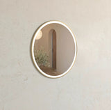 Round wall mirror with gold frame on a light gray wall
