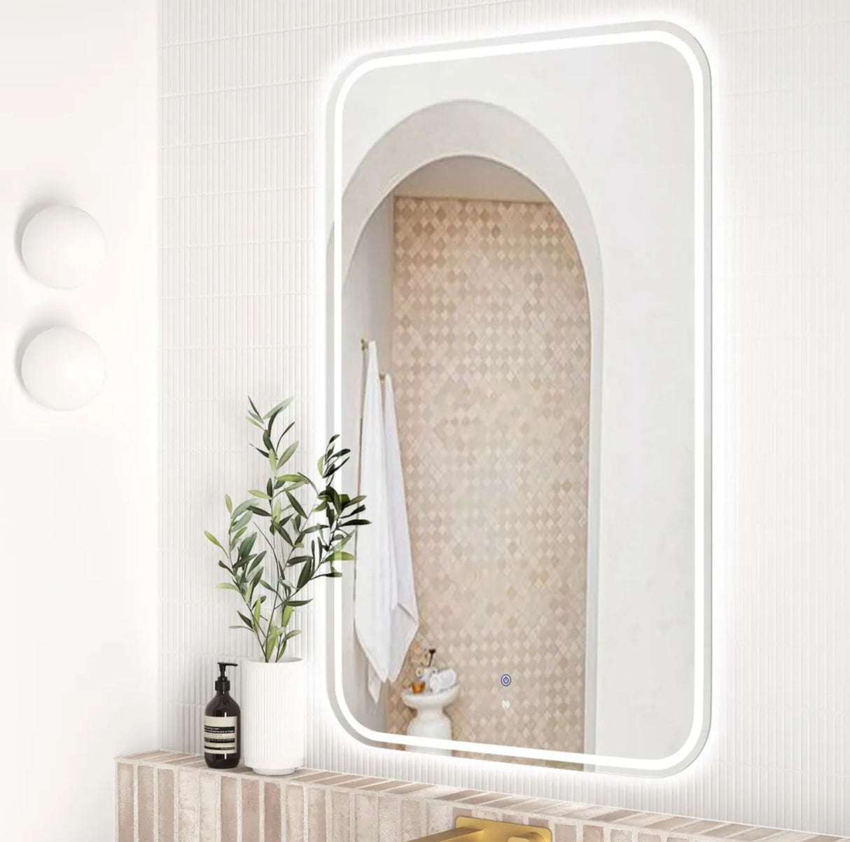 Bathroom with a large mirror reflecting a tiled wall, plant, and toiletries.
