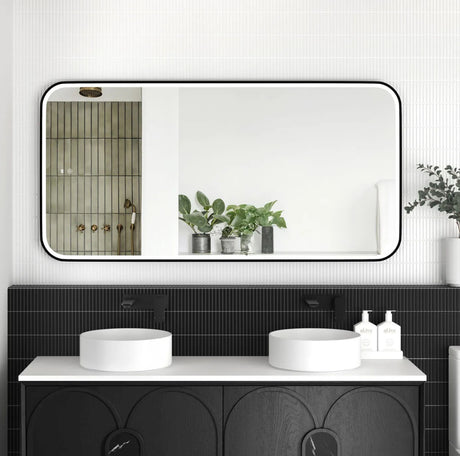 Bathroom vanity with black tiles, white countertop, and large mirror reflecting a shower area.