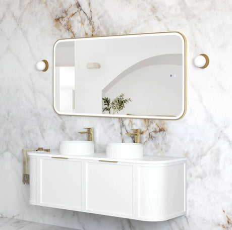 Bathroom vanity with white sinks and gold fixtures against a marble wall.