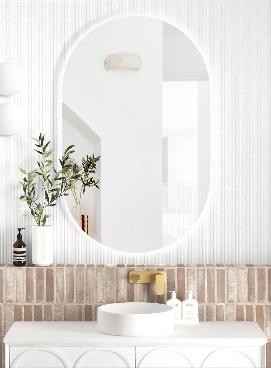 LED Noosa frameless mirror (1200x750) with a clean, curved design, mounted above a vanity with a brick-textured backsplash. The setup highlights a gold faucet, white basin, and a combination of modern and natural decorative elements.