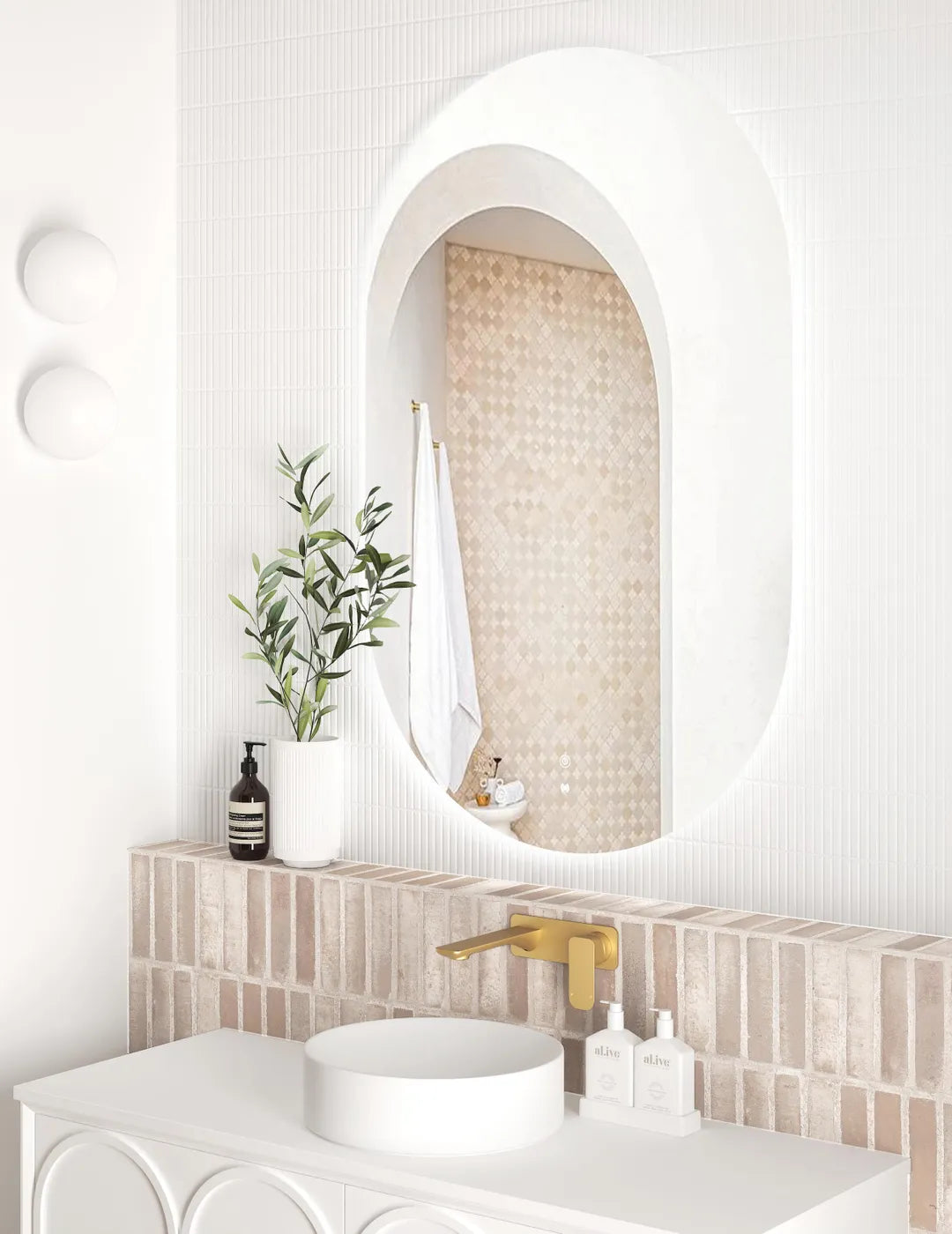 Side view of the LED Noosa 1200x750 frameless mirror, emphasizing its curved edges and ambient lighting. The bathroom includes a white basin, gold faucet, and a brick backsplash, blending warm and contemporary tones.