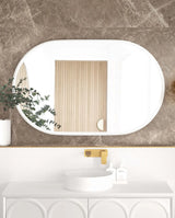 LED Noosa 1200x750 mirror with a white metal frame, featured against a luxurious marble-textured wall. The setup includes a round basin, gold faucet, and a mix of textured materials, blending modern and classic design elements.