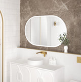 Side view of the LED Noosa 1200x750 mirror with a white metal frame, showcasing its frameless design and soft ambient lighting. The bathroom features a round basin, gold faucet, and natural greenery, offering a contemporary and refined look.