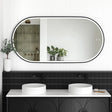 LED Noosa mirror (1500x750) with a sleek black metal frame, mounted above a modern black vanity featuring arched detailing. The bathroom setup includes dual round basins, matte black faucets, and greenery accents, creating a striking monochromatic design.