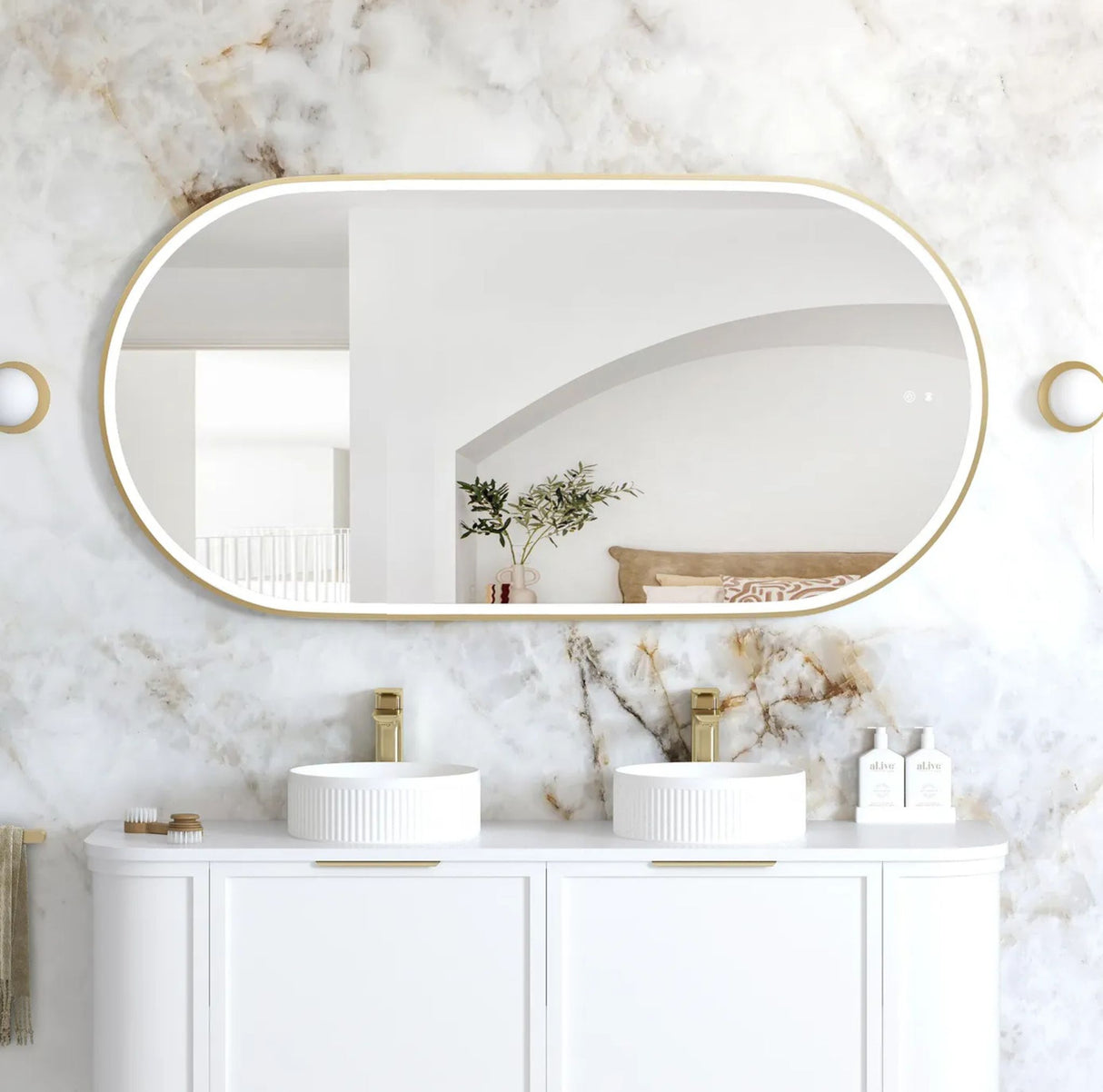 Bathroom with marble walls, oval mirror, and white vanity with sinks.