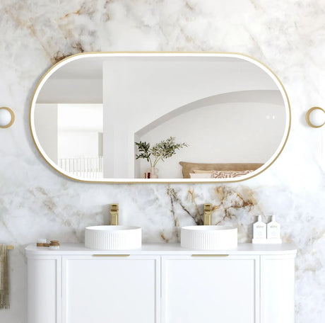 Bathroom with marble walls, oval mirror, and white vanity with sinks.
