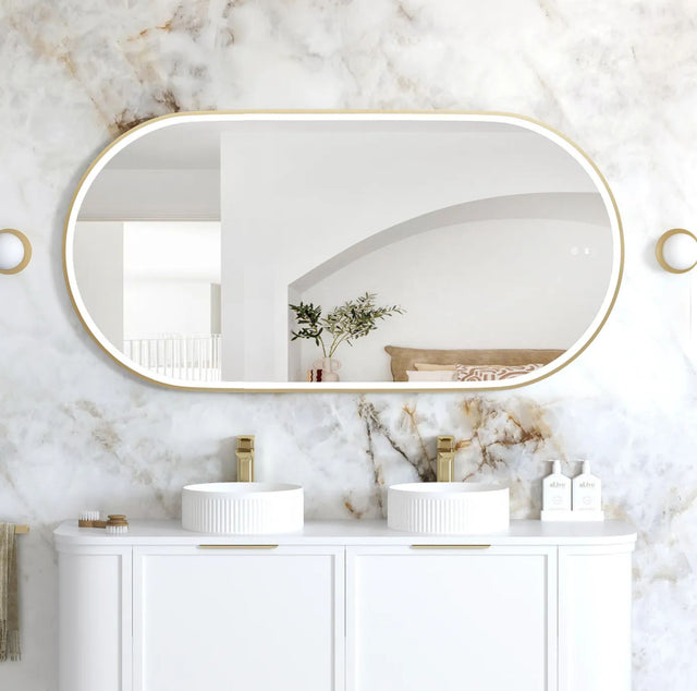 Bathroom with marble walls, oval mirror, and white vanity with sinks.
