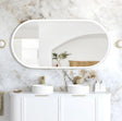Bathroom vanity with two sinks, mirrors, and decorative items against a marble wall.