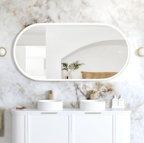 Bathroom vanity with two sinks, mirrors, and decorative items against a marble wall.
