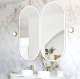 Bathroom with marble walls, two oval mirrors, and a sink.