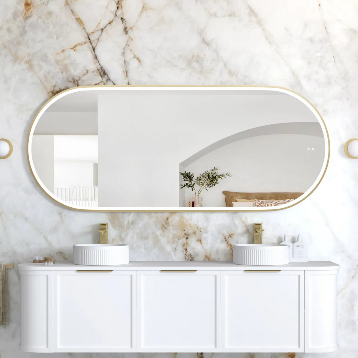 Bathroom vanity with white cabinets, marble countertop, and large oval mirror on a marble wall.